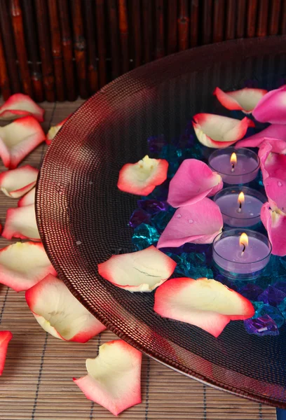 Płatki róż i świece w wodę w wazonie na drewnianym stole na drewniane tła — Zdjęcie stockowe