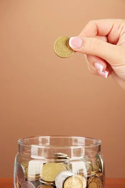 Sparen, weibliche Hand steckt eine Münze in Glasflasche, auf farbigem Hintergrund — Stockfoto