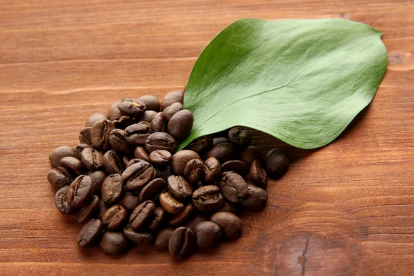Κόκκους καφέ με φύλλα σε ξύλινα φόντο — Φωτογραφία Αρχείου