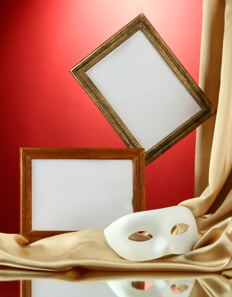 White mask, empty frames and golden silk fabric, on red background — Stock Photo, Image