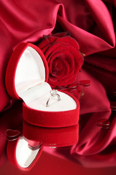 Beautiful box with wedding ring and rose on red silk background