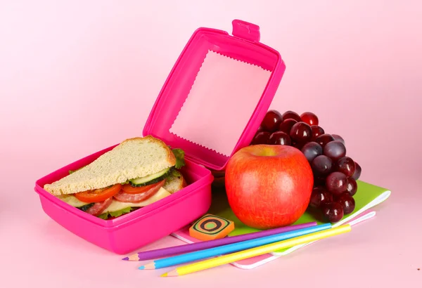 Almoço com sanduíche, frutas e artigos de papelaria sobre fundo rosa — Fotografia de Stock