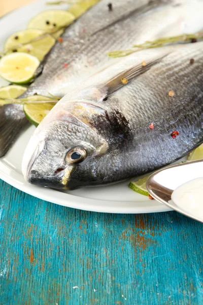 Two fish dorado with lemon on plate on blue wooden table close-up — Stock Photo, Image
