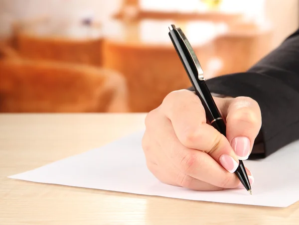 Hand met pen op wit papier, op houten tafel op lichte achtergrond Stockfoto