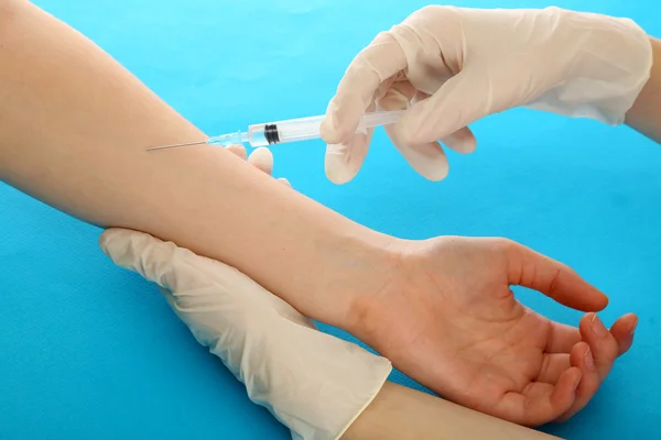 Läkare anläggning spruta med vaccin i patientens hand, på blå bakgrund — Stockfoto