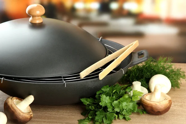 Black wok pan and mushrooms on kitchen wooden table, close up — Stock Photo, Image