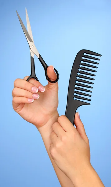 Color comb and scissors in female hand on color background — Stock Photo, Image