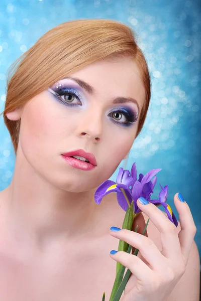 Piękna młoda kobieta z seksowny makijaż i kwiat na niebieskim tle — Zdjęcie stockowe