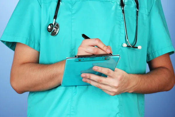 Hand of doctor with pen writing on prescription blank, on blue background — Stock Photo, Image