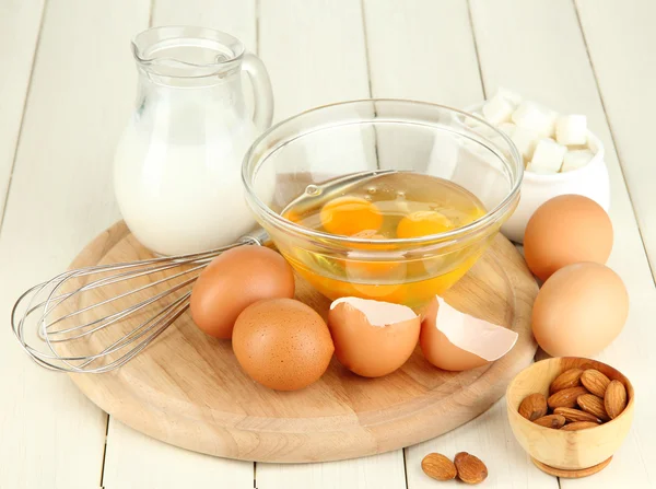 Broken egg in bowl and various ingredients next to them on wooden table close-up — Stock Photo, Image