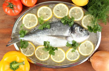 dorado fresco en tajadera con limón y verduras en la mesa de madera