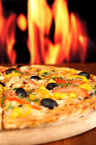 Delicious pizza close-up on wooden table on fire background — Stock Photo, Image