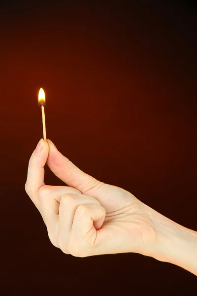 Burning match in female hand, on dark brown background — Stock Photo, Image