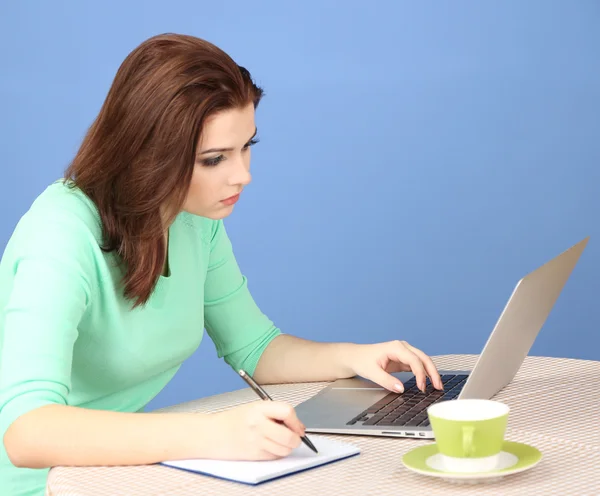 Mooie jonge vrouw die op laptop op blauwe achtergrond werkt — Stockfoto