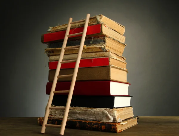 Oude boeken en houten ladder, op grijze achtergrond — Stockfoto