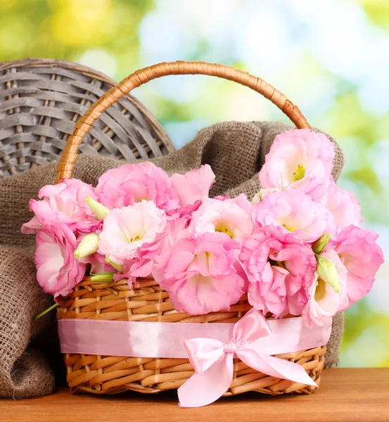 Boeket van eustoma bloemen in mand, op houten tafel, op groene achtergrond — Stockfoto