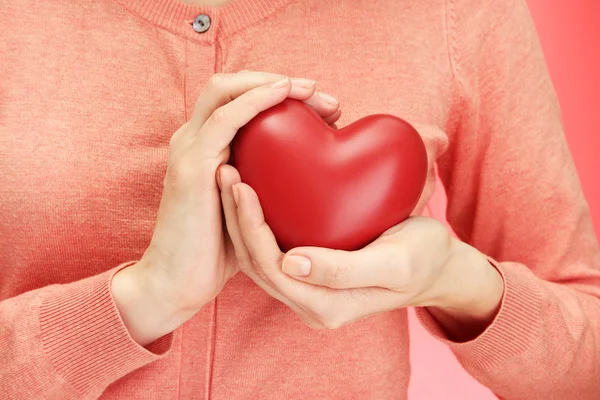 Corazón rojo en manos de mujer, sobre fondo rojo — Foto de Stock