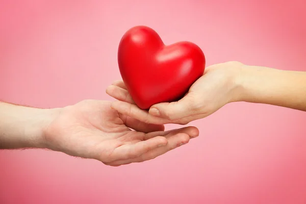 Red heart in woman and man hands, on pink background — Stock Photo, Image