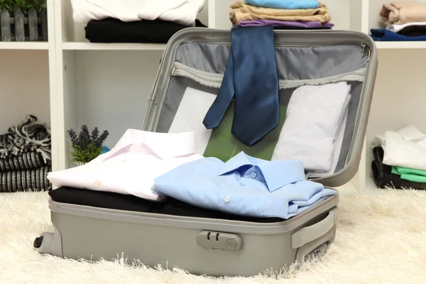 Open grey suitcase with clothing in room — Stock Photo, Image