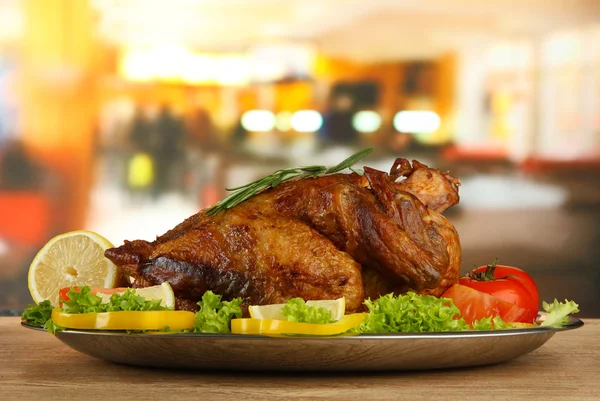 Whole roasted chicken with vegetables on plate, on wooden table in cafe — Stock Photo, Image