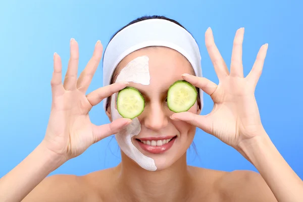 Mujer joven con máscara facial de arcilla, sobre fondo azul —  Fotos de Stock