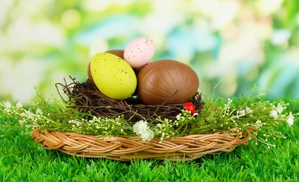 Composizione di uova di Pasqua e cioccolato in nido su erba su sfondo naturale — Foto Stock