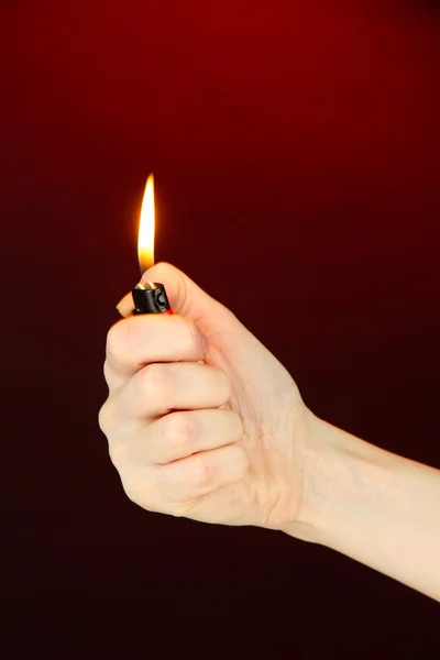 Burning lighter in female hand, on dark red background — Stock Photo, Image