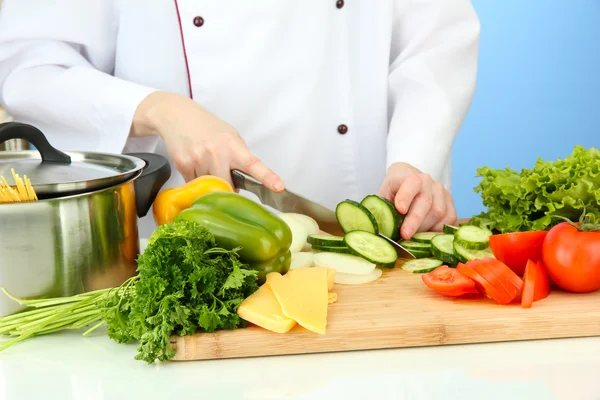 Женские руки режут овощи, на синем фоне — стоковое фото