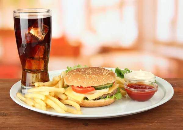 Tasty cheeseburger with fried potatoes and cold drink, on bright background — Stock Photo, Image
