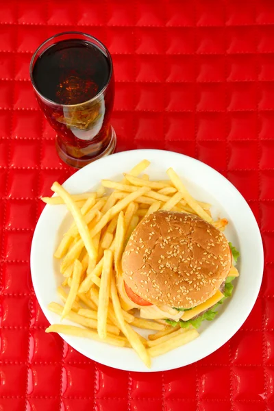 Tasty cheeseburger with fried potatoes and cold drink, on red background — Stock Photo, Image