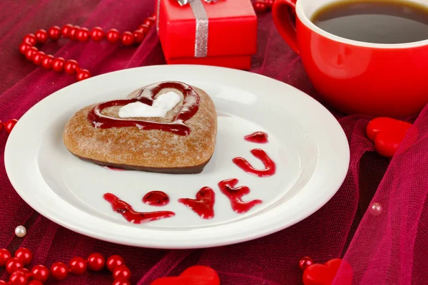 Biscotto al cioccolato a forma di cuore con tazza di caffè sulla tovaglia rosa primo piano — Foto Stock