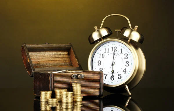 Reloj despertador con monedas en el pecho sobre fondo oscuro —  Fotos de Stock