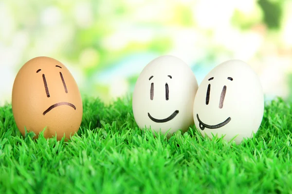 Eggs with funny faces on grass on bright background — Stock Photo, Image