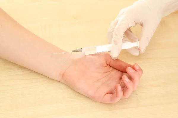 Médico sosteniendo la jeringa con una vacuna en la mano del paciente, sobre fondo de madera — Foto de Stock