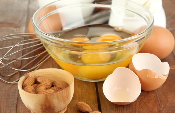 Zerbrochenes Ei in Schüssel und verschiedene Zutaten daneben auf Holztisch in Großaufnahme — Stockfoto