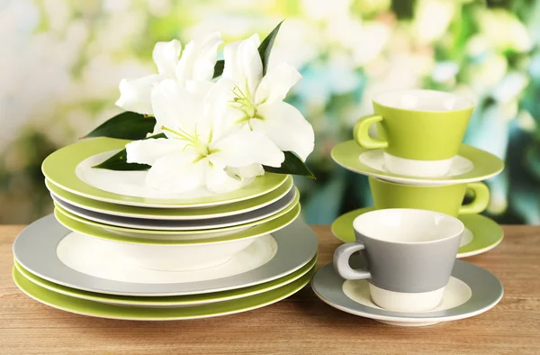 Empty plates and cups on wooden table on green background — Stock Photo, Image