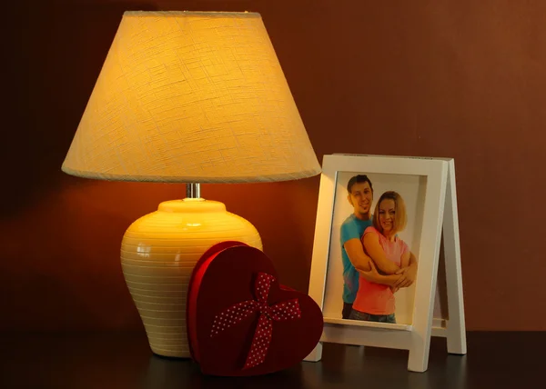 Bílý fotorámeček a lampu na dřevěný stůl na pozadí hnědé stěny — Stock fotografie