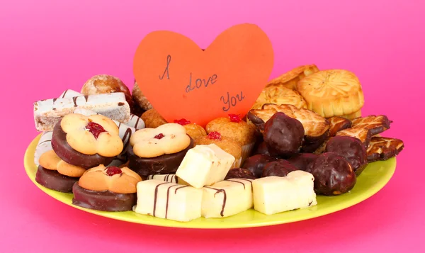 Sweet cookies on plate with valentine card on pink background Stock Image