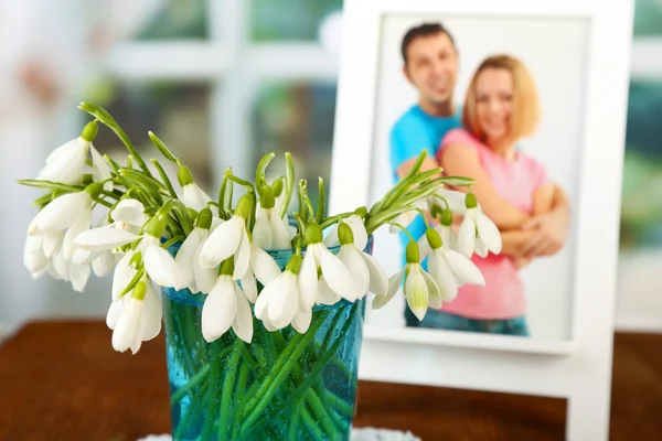 スノー ドロップ木製テーブル、明るい背景上のガラスの花瓶に花の花束 — ストック写真