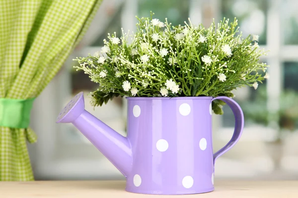 Decorative flowers in watering can on windowsill — Stock Photo, Image