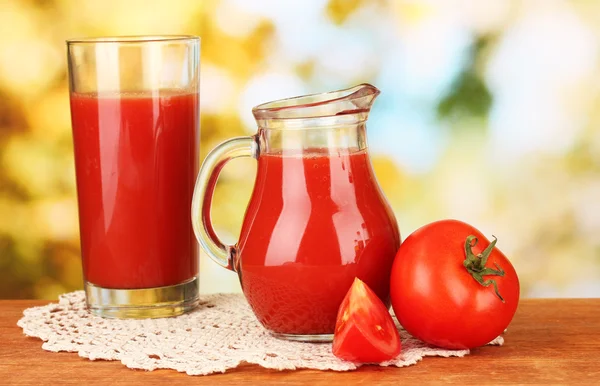 Jarra llena de jugo de tomate, sobre mesa de madera sobre fondo brillante — Foto de Stock