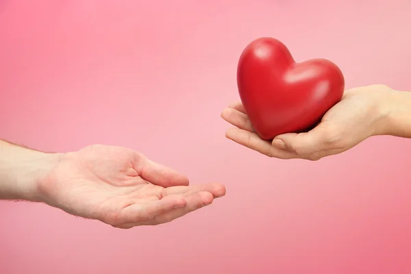 Red heart in woman and man hands, on pink background — Stock Photo, Image