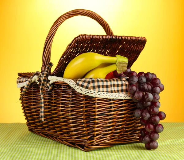 Picnic basket with fruits on cloth on yellow background — Stock Photo, Image