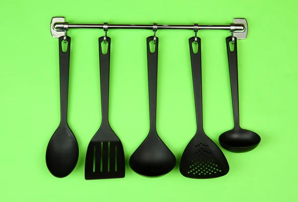 Black kitchen utensils on silver hooks, on green background — Stock Photo, Image
