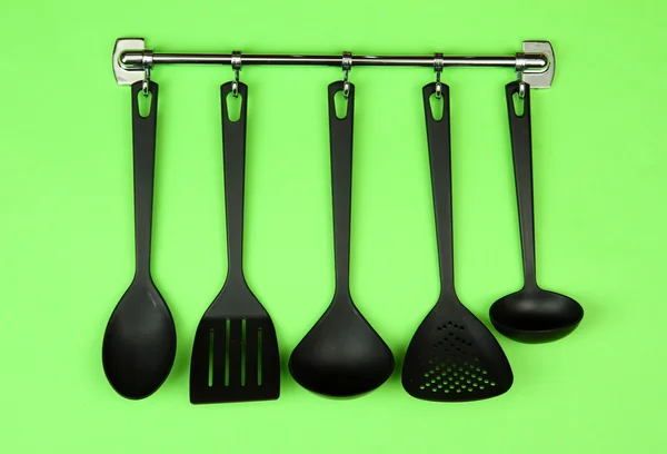 Utensílios de cozinha preto em ganchos de prata, no fundo verde — Fotografia de Stock