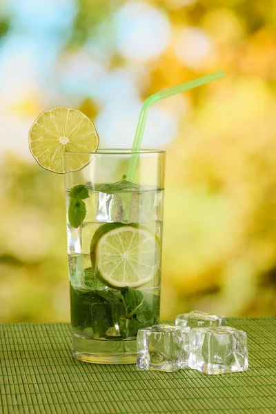 Bicchiere d'acqua con ghiaccio, menta e calce sul tavolo su sfondo luminoso — Foto Stock