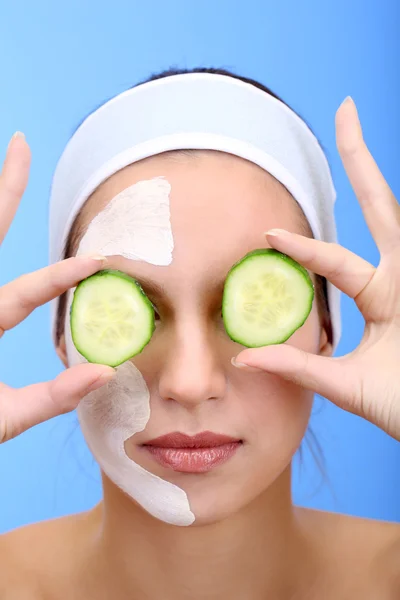 Mujer joven con máscara facial de arcilla, sobre fondo azul —  Fotos de Stock