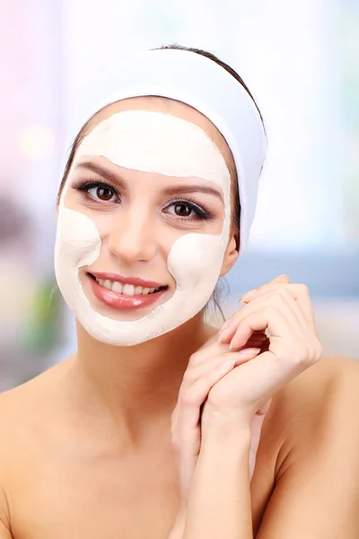 Jeune femme avec masque facial en argile, sur fond lumineux — Photo