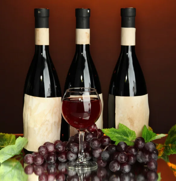 Composizione di bottiglie di vino, vetro e uva, su fondo rosso scuro — Foto Stock