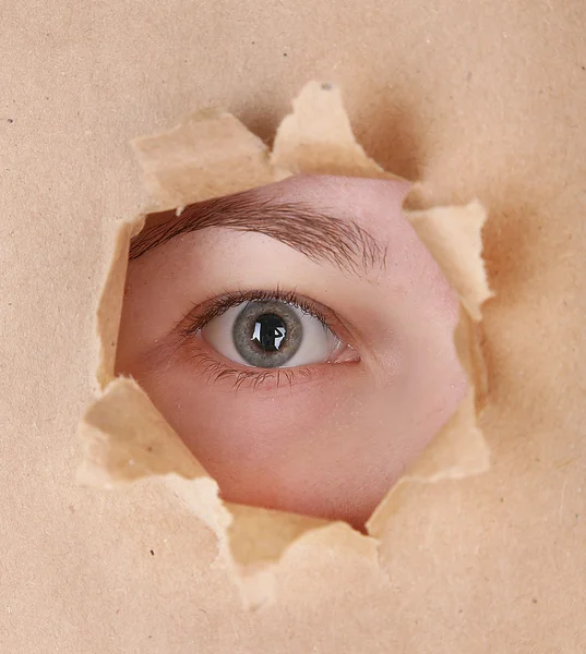 Female eye looking through hole in sheet of paper — Stock Photo, Image